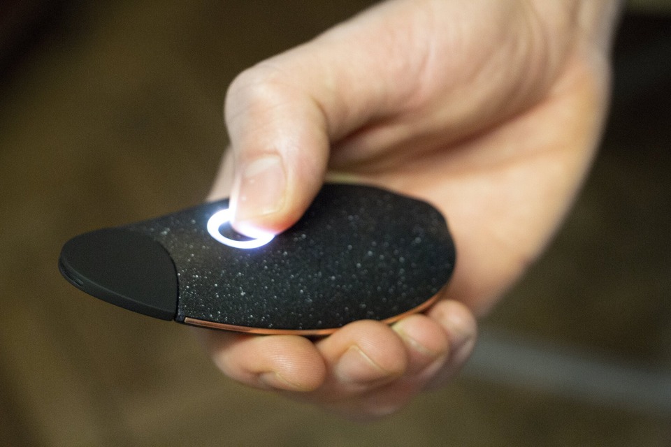 A hand holding the prototype with the thumb pressing the button, which is glowing white